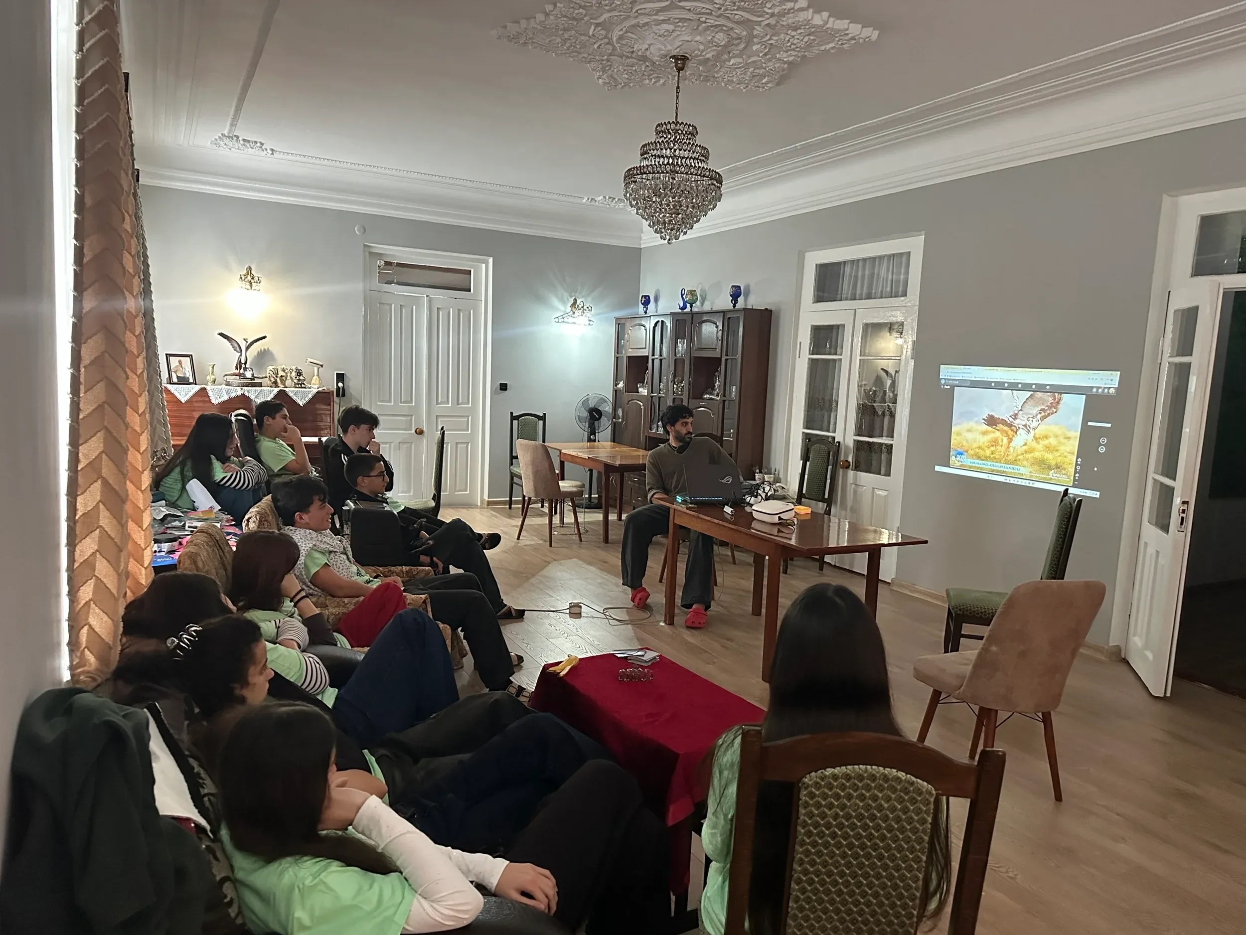 Öğrenciler bir odada oturmuş, duvara yansıtılan yırtıcı kuş fotoğrafını izliyor.